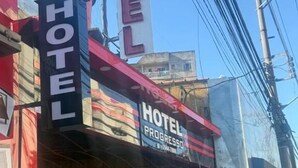 Un hotel con un cartel llamativo que dice "HOTEL PROGRESSO" y una entrada visible con una puerta blanca y un bote de basura afuera.