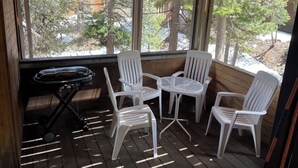 Ein überdachter Außenbereich mit Grill, weißen Plastikstühlen und einem Tisch.