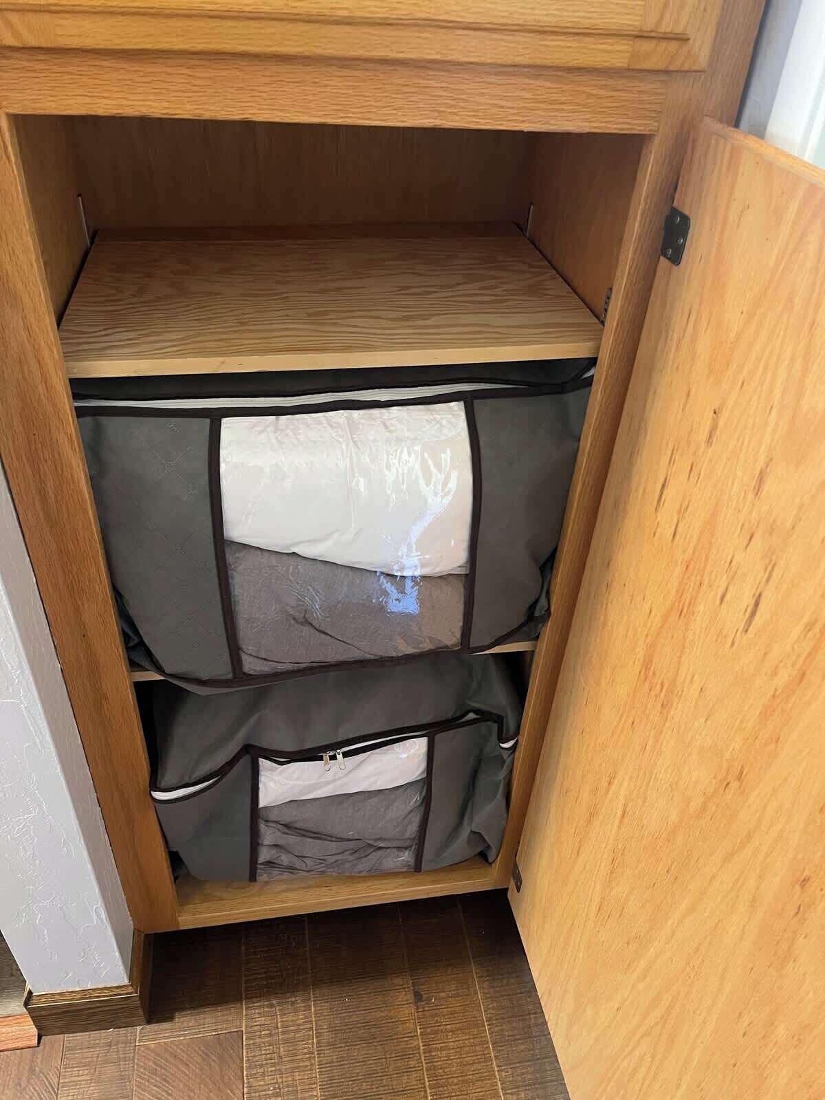 A wooden cabinet with three drawers, each containing a grey fabric item.