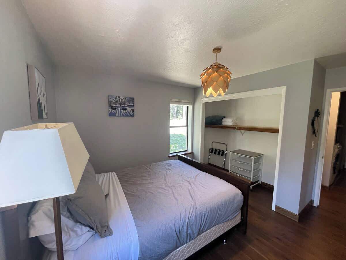 Une chambre à coucher avec un lit, un bureau avec une lampe, un luminaire suspendu et une fenêtre.