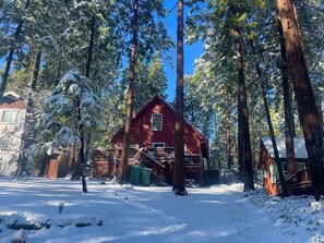 A red cabin surrounded by tall pine trees in a snowy landscape. - Cottage in the Pines – Cabin w/ Lake Access & Fenced Yard in Twain Harte (Twain Harte)