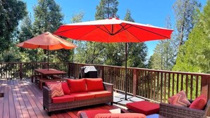 Een houten terras met rieten meubels, rode kussens en twee rode parasols.