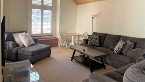 Een woonkamer met een houten plafond, een grijze bank, een salontafel en een televisie.