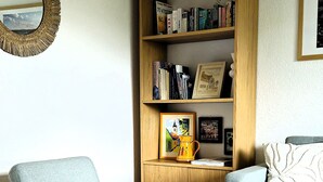 A living room with a blue armchair, a wooden bookshelf, a grey sofa, and a white rug.