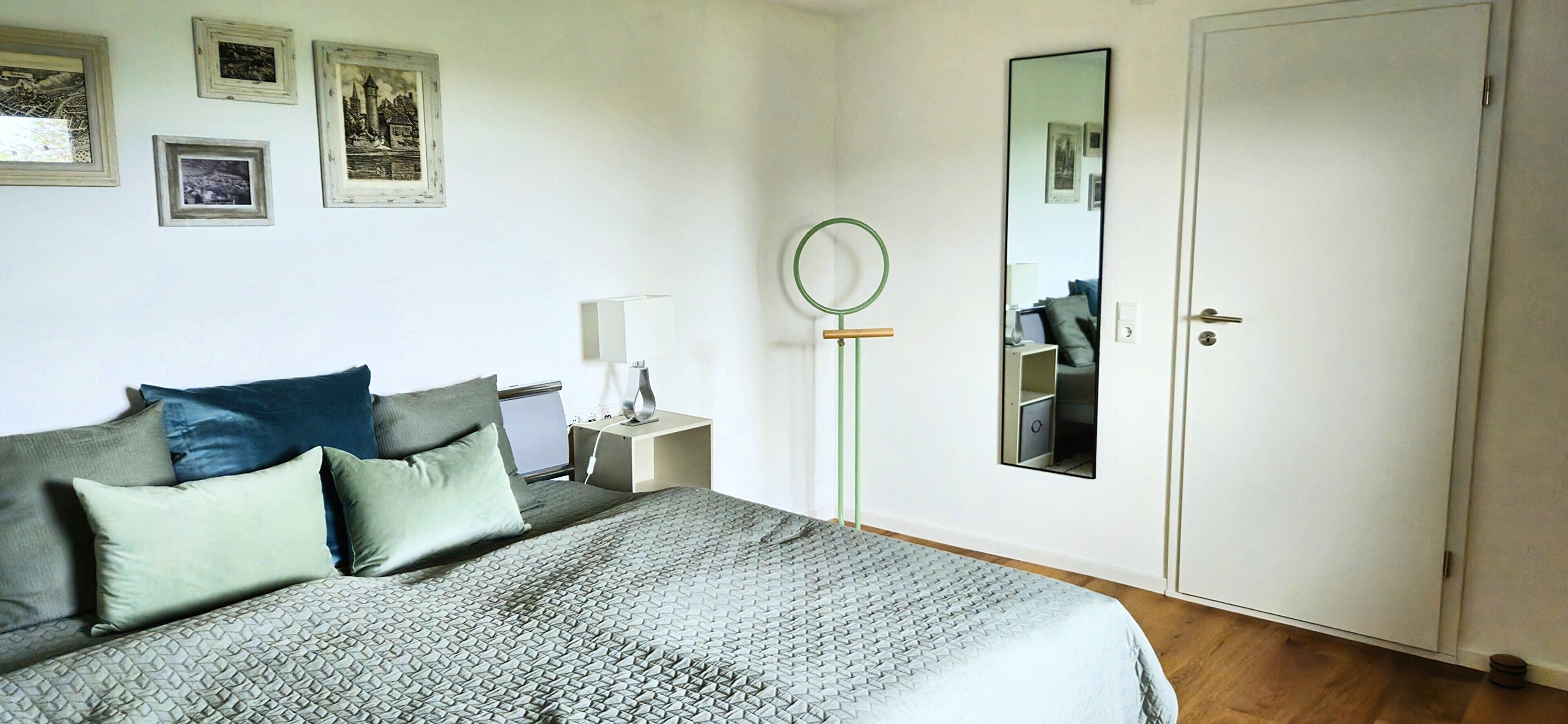 Ein Schlafzimmer mit Bett, Nachttisch, Lampe, Spiegel und einer Tür.