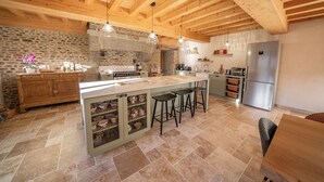 A spacious kitchen with a large island, stone walls, and wooden beams. - Les CLEFS de la Baie- Charming house for 12 people in the Bay of Mont Saint Michel (Céaux)