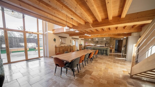 A spacious dining area with a long wooden table and chairs, a kitchen in the background, and a staircase leading to an upper level. - Les CLEFS de la Baie- Charming house for 12 people in the Bay of Mont Saint Michel (Céaux)