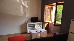 A compact living space with a white desk, a black sofa, a red cushion, and a window with a view of greenery. - Country house - Ideal for a team of workers (Nérac)