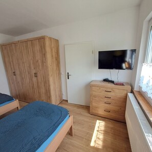 Ein Schlafzimmer mit Holzschrank, Fernseher, Nachttisch und einem Fenster mit Vorhängen.