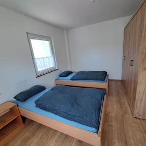 Ein kleines Schlafzimmer mit einem Einzelbett, einem Holzschrank, einem kleinen Tisch und einem Fenster mit Vorhang.