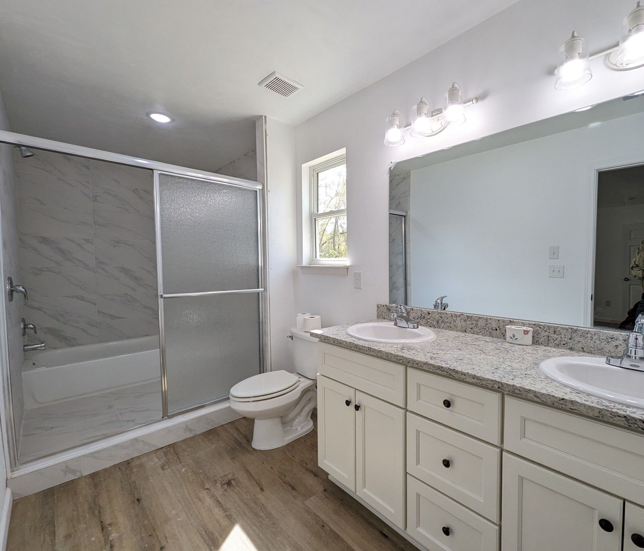 A modern bathroom with a walk-in shower, two sinks, a toilet, and a large mirror.