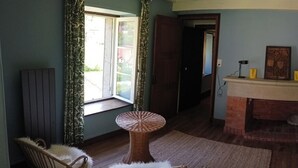 Un dormitorio con una cama, chimenea, ventana con cortinas, una silla y una mesita.