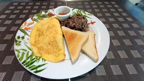 A plate with a fried egg, two slices of toast, and a small bowl of sauce on a table with a patterned tablecloth. - Corcovado Pura Vida Stays (Puerto Jiménez)