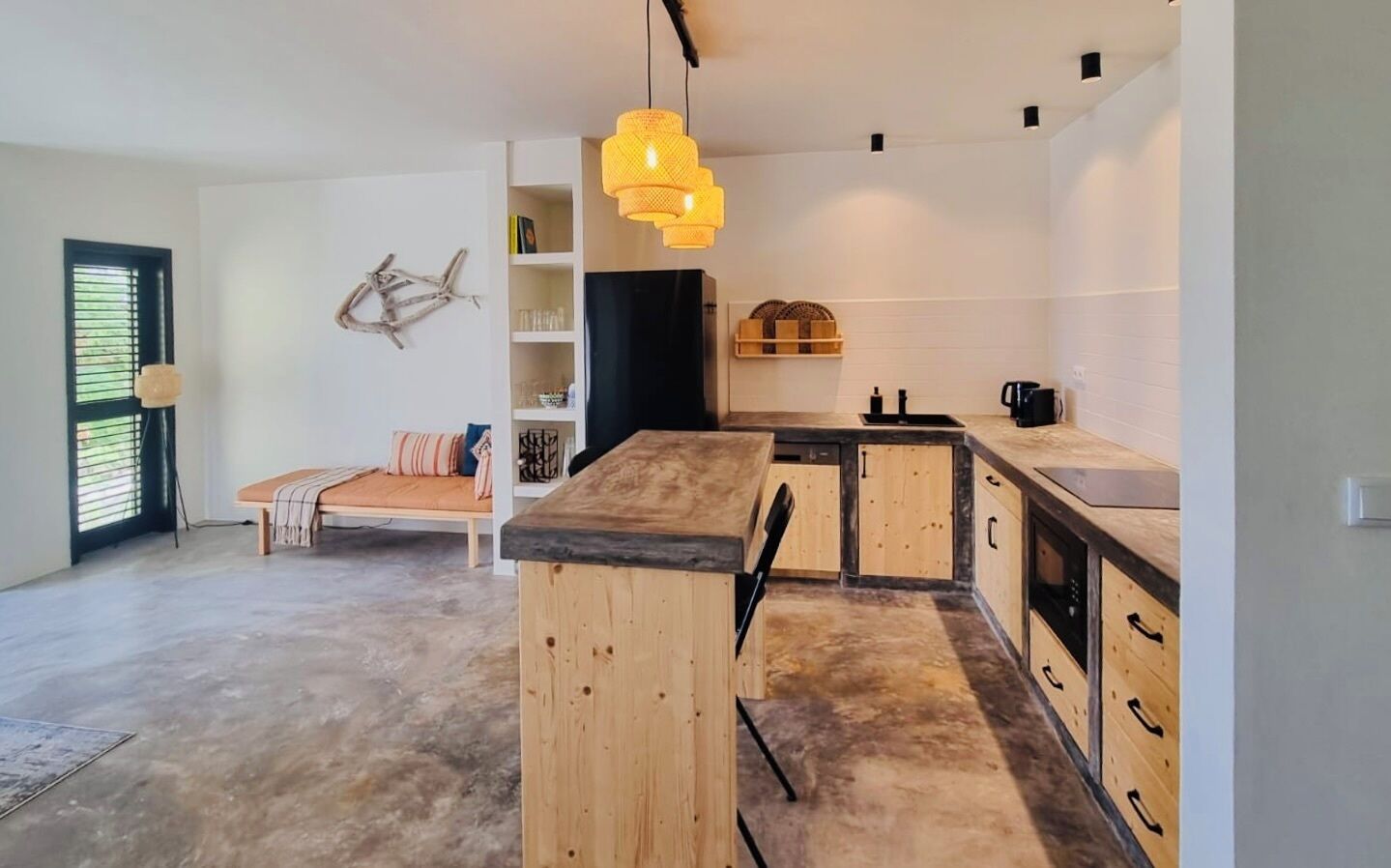 Une cuisine moderne avec des meubles en bois et un îlot central, un coin repas avec un banc, et une étagère murale agrémentée d’objets décoratifs.