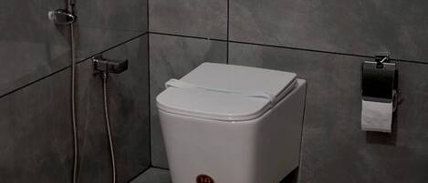 Une petite salle de bain avec des toilettes blanches, une douche et un distributeur de serviettes.