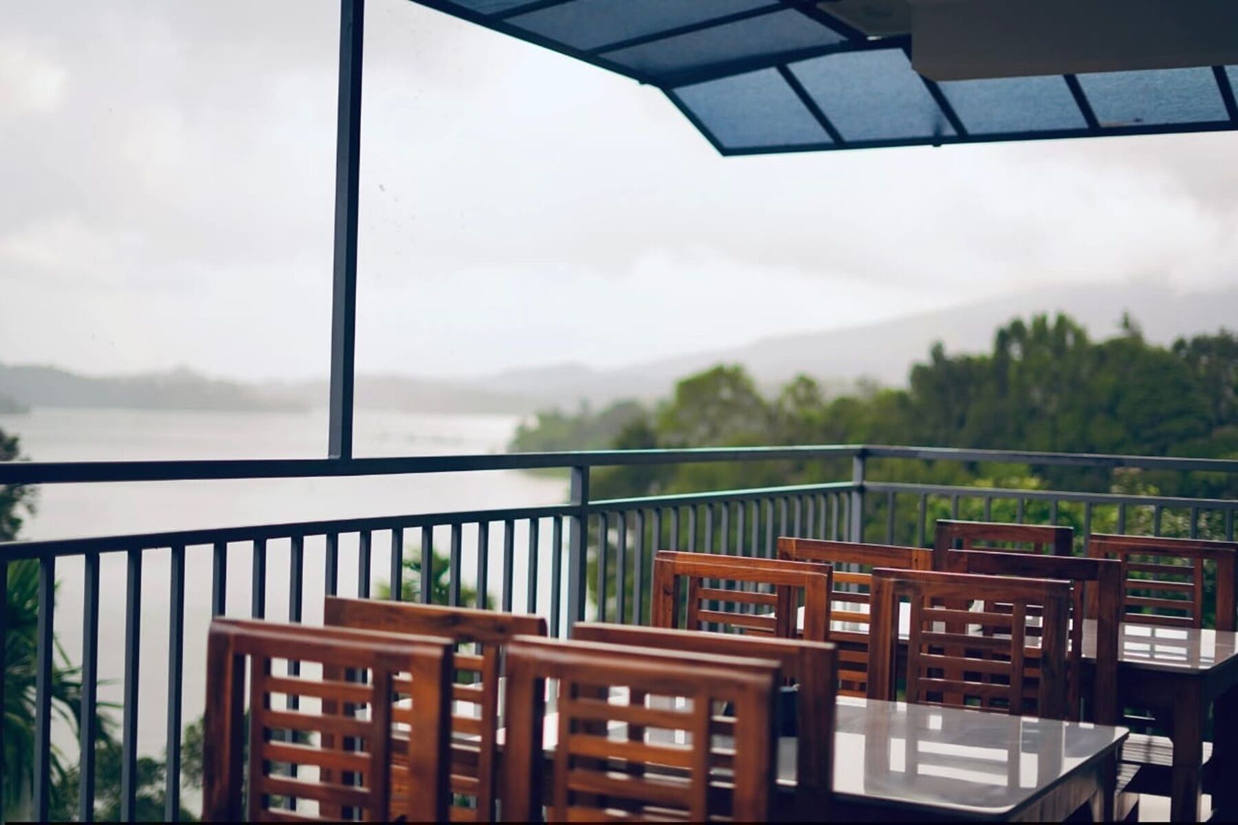 Una terraza con sillas y mesas de madera, con vista a un cuerpo de agua y vegetación.