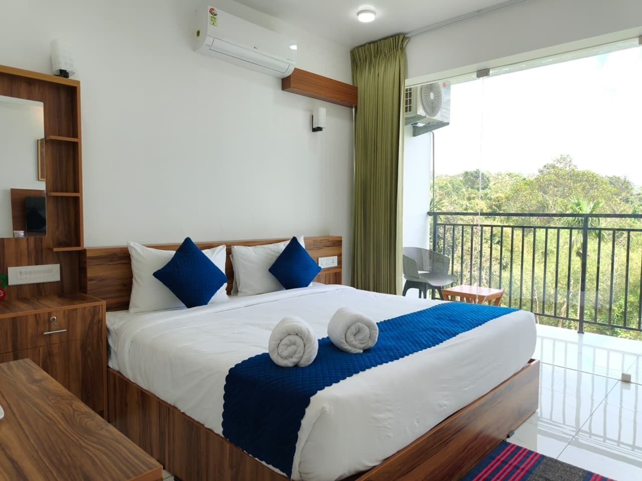 Una camera d'albergo con un letto grande, una testiera in legno, una scrivania piccola e un balcone con vista sugli alberi.