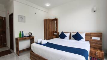A bedroom with a wooden bed frame, a nightstand, a wooden wardrobe, and a desk with a kettle and bottles.