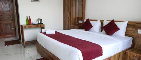 A hotel room with a large bed, wooden headboard, a bedside table with a kettle, and a nightstand.