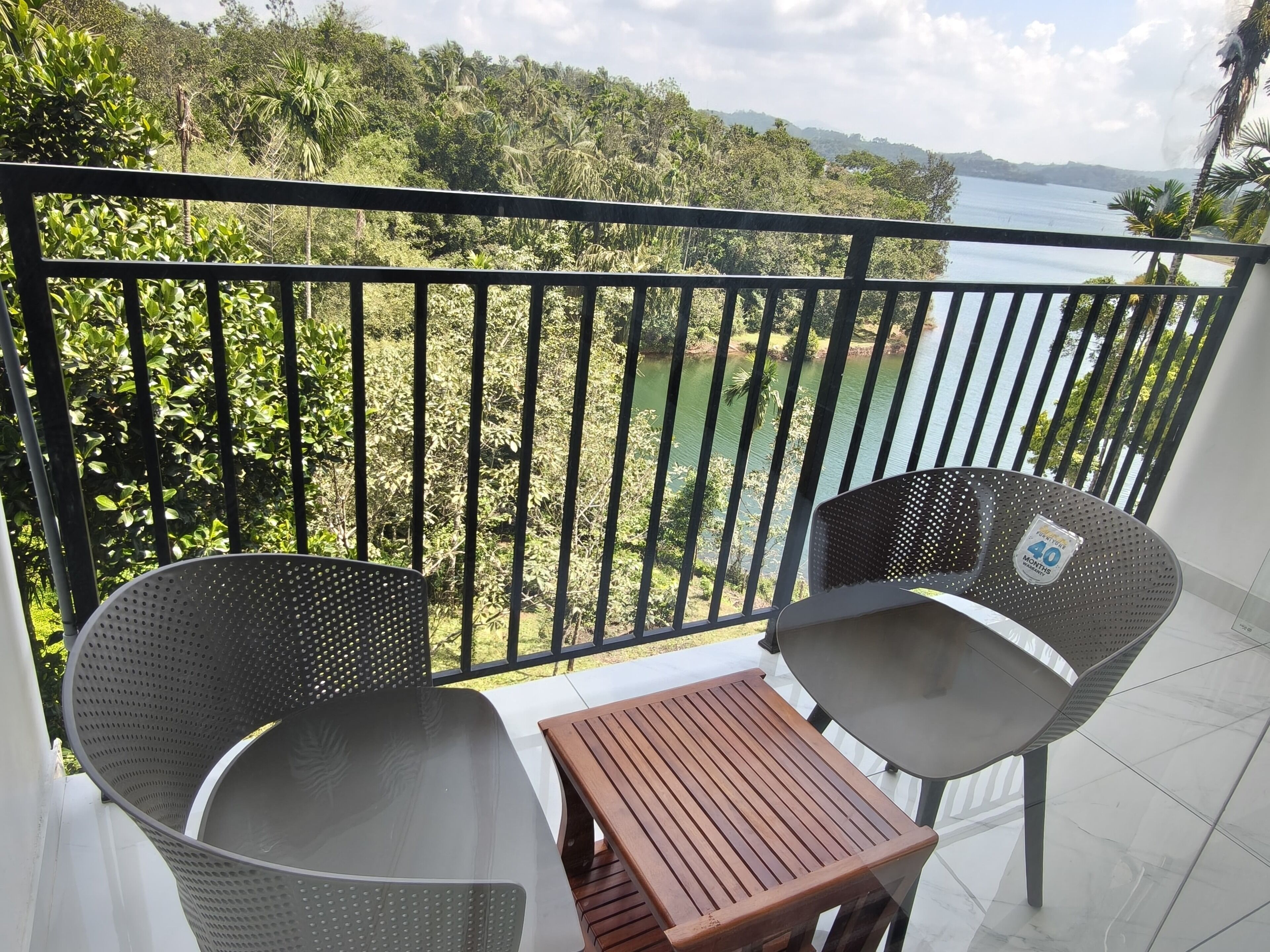A balcony with two chairs and a small table, overlooking a lush green landscape and a body of water.