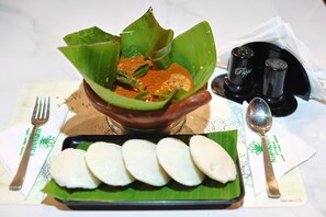 Un plat traditionnel servi dans un pot en argile, accompagné d’une feuille de bananier et d’une assiette de riz blanc.