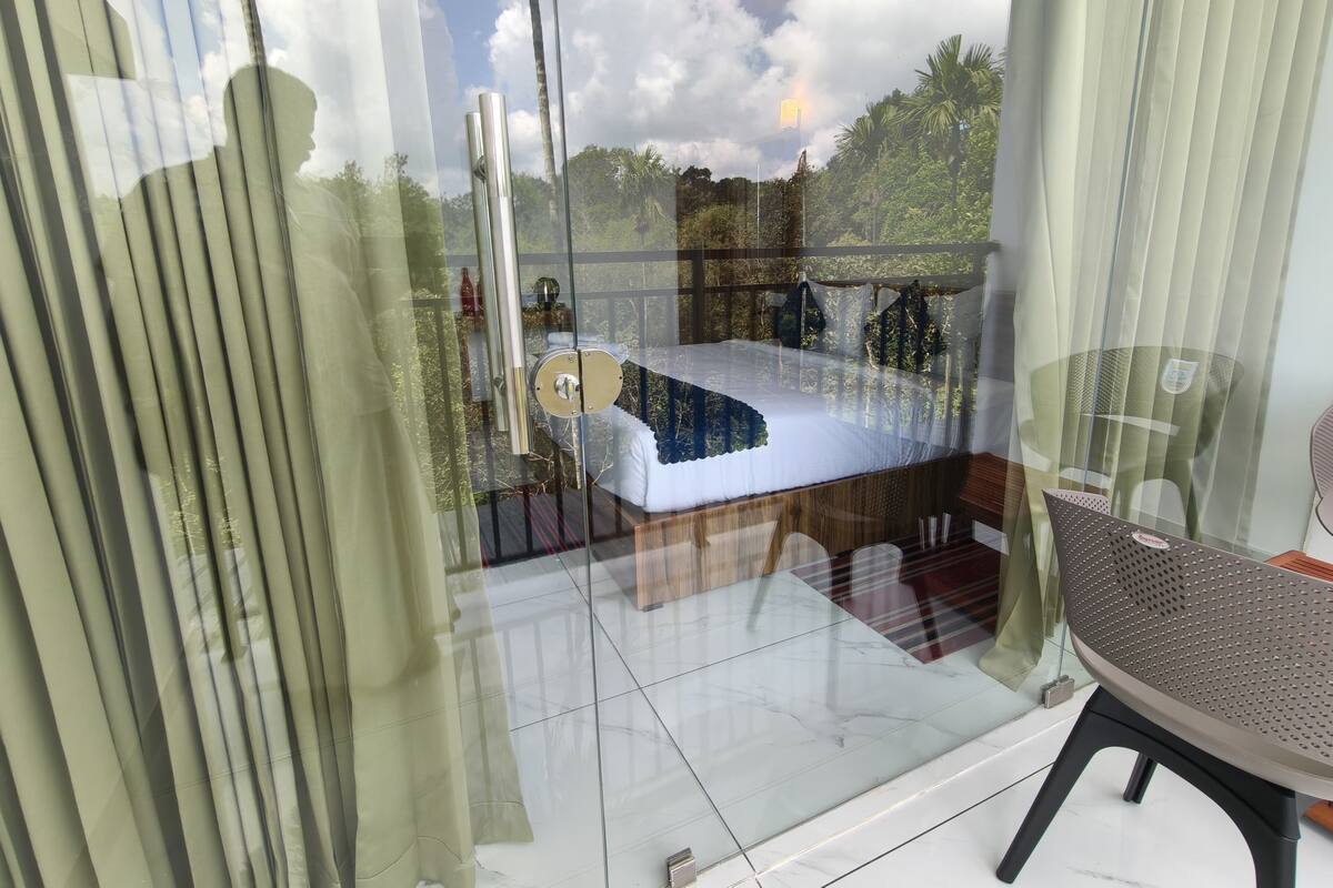 Un dormitorio con cama, una silla y vistas al exterior a través de un ventanal.