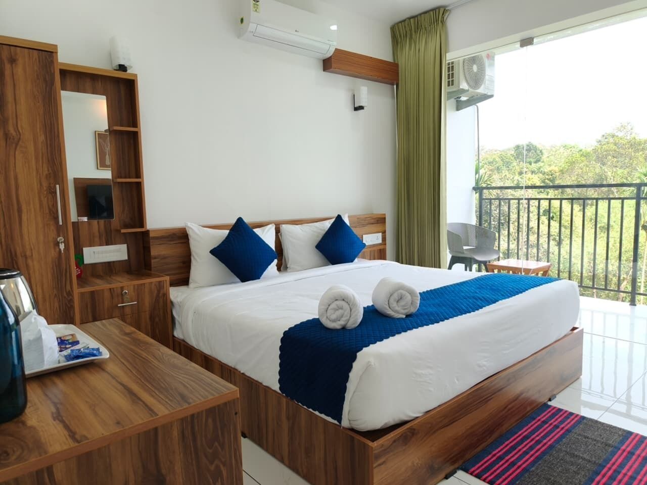 Une chambre d’hôtel avec un lit en bois, une table de chevet en bois, un bureau et un balcon donnant sur un paysage verdoyant.