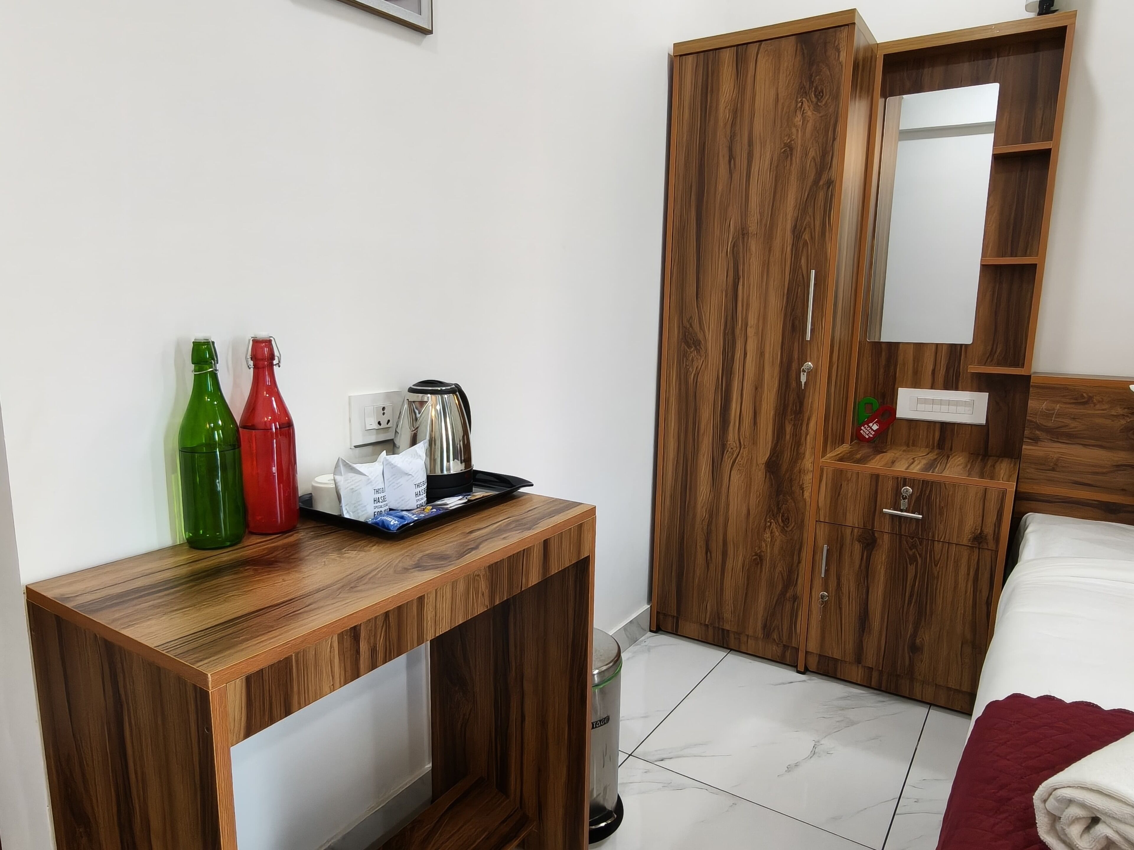 A hotel room with a wooden desk, a bed, a wardrobe, and a mirror.