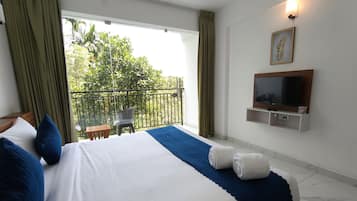 A hotel room with a bed, a TV, a balcony with a view of greenery, and a small table.