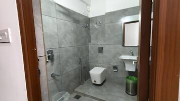 Un baño moderno con azulejos grises, una ducha, un inodoro, un lavabo y un cubo de basura.