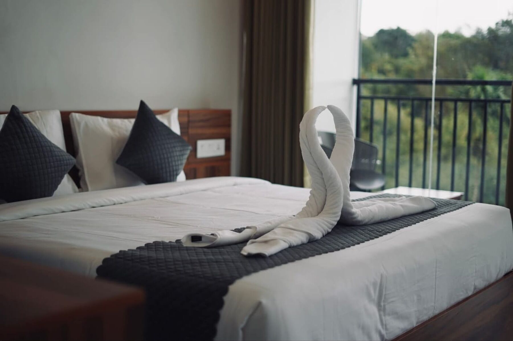 Een net opgemaakt bed met een handdoek gevouwen in de vorm van een zwaan, een zwarte plaid en een houten hoofdbord.