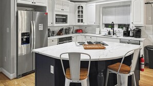 Uma cozinha moderna com armários brancos, eletrodomésticos de aço inoxidável, uma ilha central com banquetas e teto de madeira.