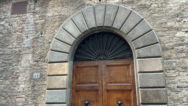 A double wooden door with a stone archway, a window above, and a brick wall. - Casa Siena Bruna, typical central apartment with breathtaking views (Siena)