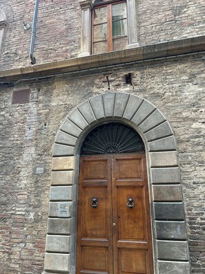 Una puerta doble de madera con arco de piedra, una ventana encima y un muro de ladrillo.