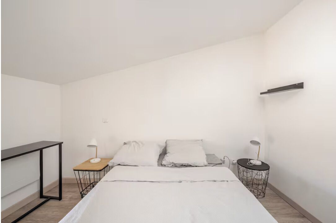 Een minimalistische slaapkamer met een bed, twee nachtkastjes en een klein bureau.