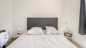 Une chambre d’hôtel avec un lit, deux tables de chevet, une lampe et un rideau.