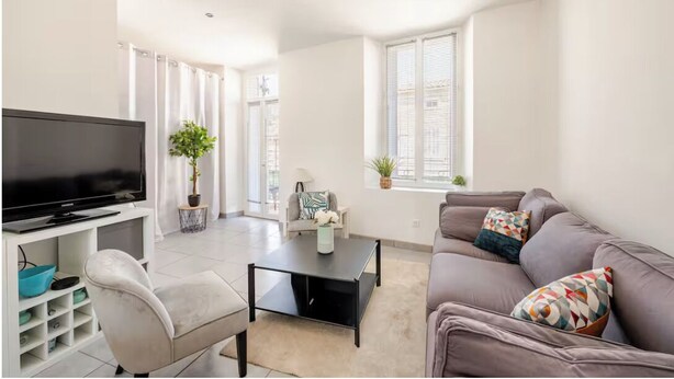 Un salon moderne avec un téléviseur à écran plat, un canapé gris, une table basse et un fauteuil blanc.