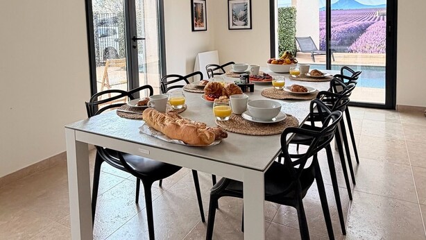 Un vaste espace dédié à la salle à manger, avec une grande table, des chaises noires et un luminaire suspendu au design moderne.