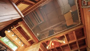 Un intérieur en bois avec un plafond haut, des poutres apparentes et une partie du plafond recouverte d’un filet.