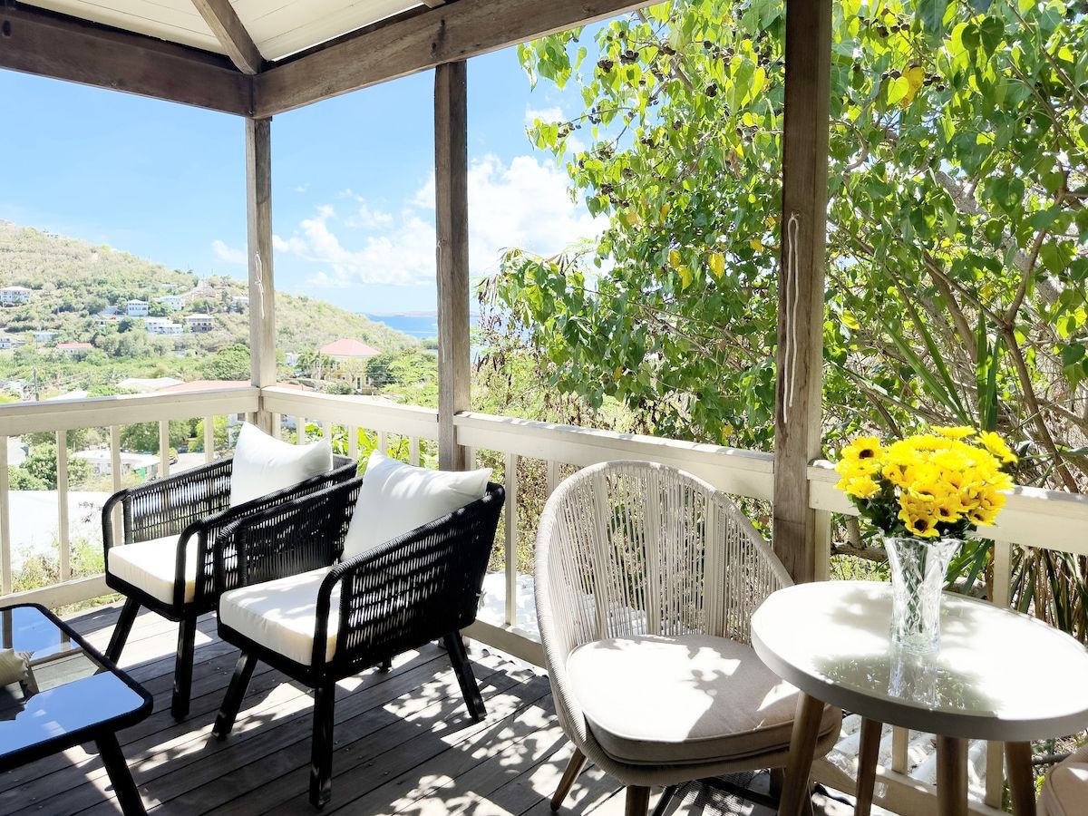 A covered outdoor seating area with wicker furniture and a table with a vase of yellow flowers.