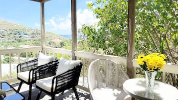 A covered outdoor seating area with wicker furniture and a table with a vase of yellow flowers.