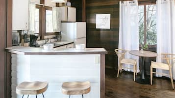 A kitchen with a central island, two bar stools, a dining table with chairs, and a window with curtains.
