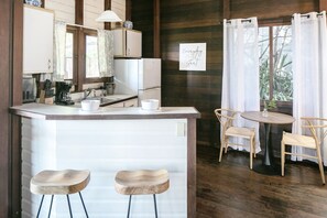 A kitchen with a central island, two bar stools, a dining table with chairs, and a window with curtains. - Oceanview Cottage Walk to Beach & Restaurants (Cruz Bay)