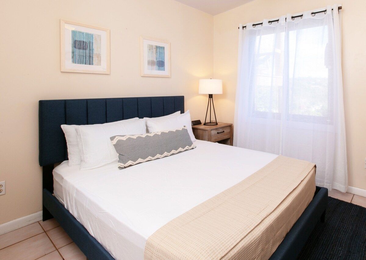 A hotel room with a bed, a nightstand, a lamp, and two framed pictures on the wall.