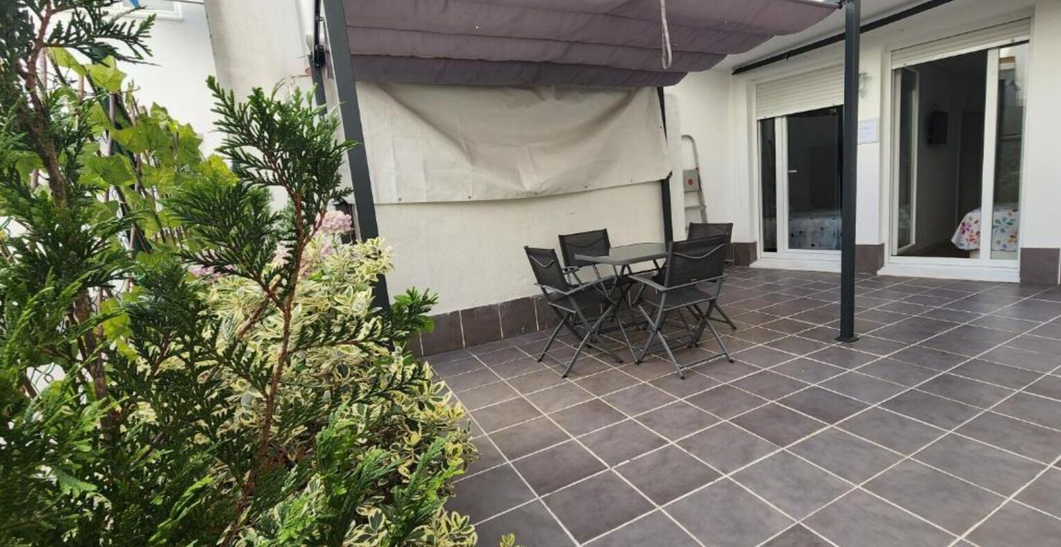 Un espace extérieur aménagé en terrasse, avec une table et des chaises, entouré de plantes en pot.