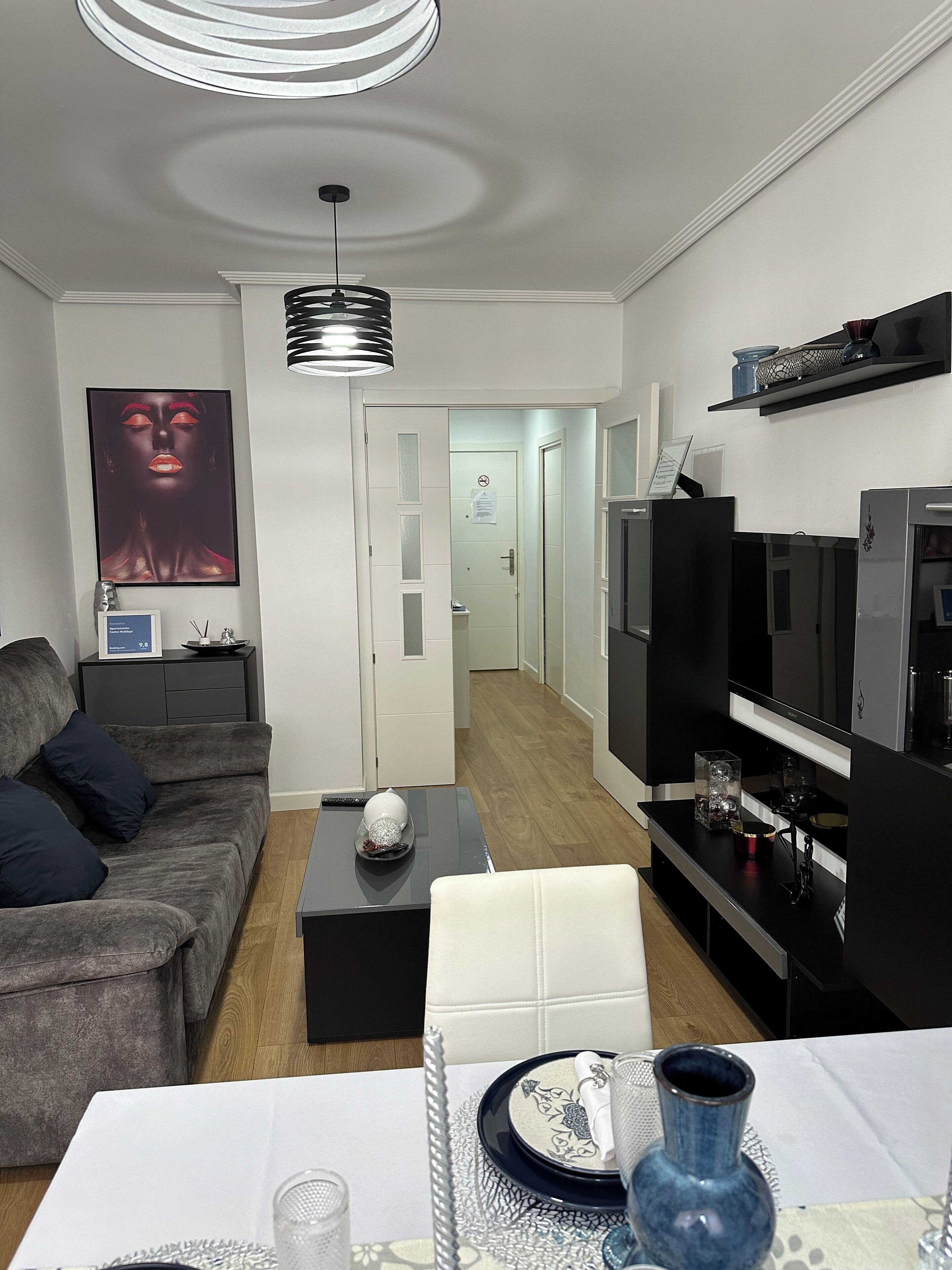 A modern living room with a grey sofa, a black coffee table, a white armchair, and a TV stand with a flat-screen TV.