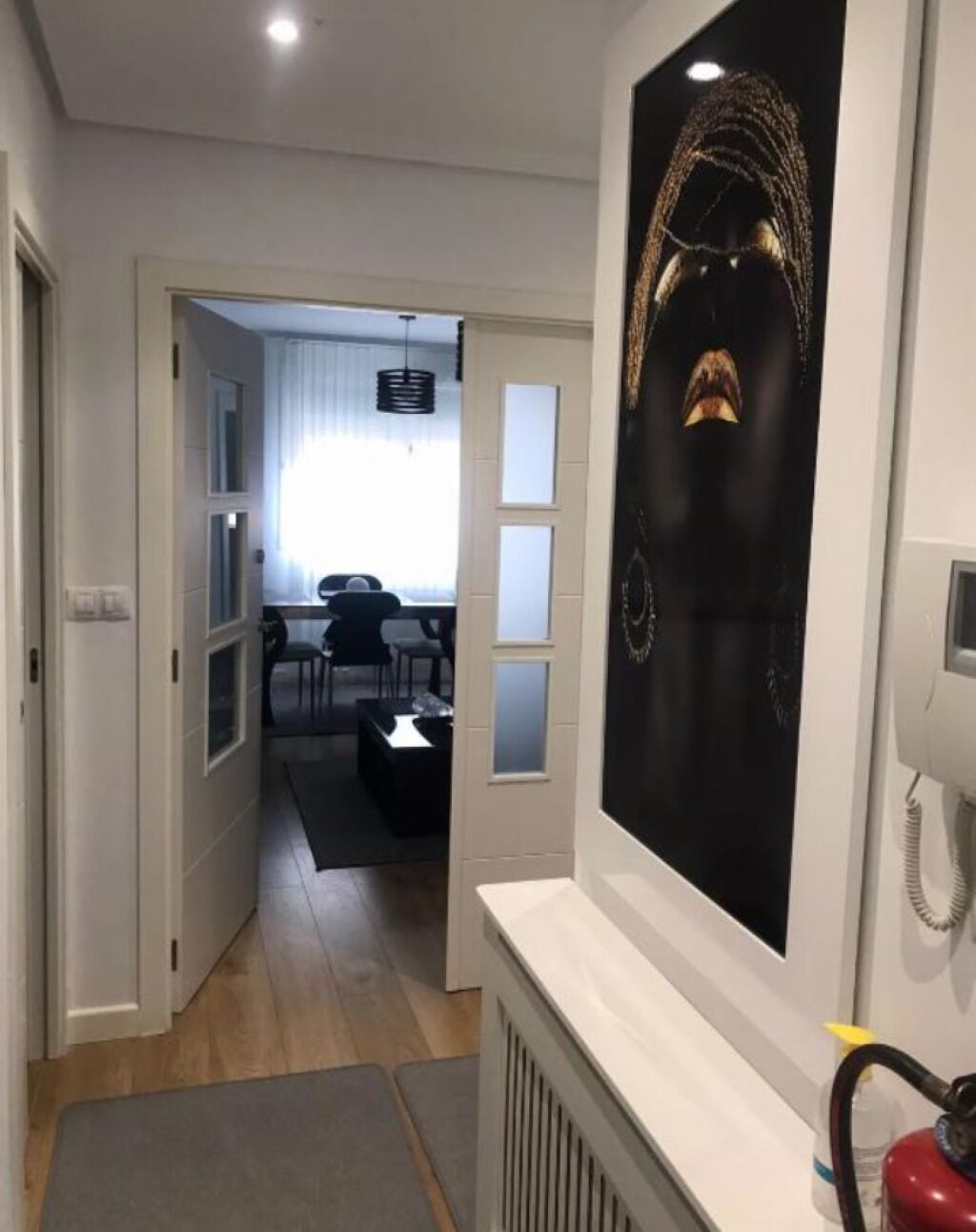 Un couloir avec un radiateur blanc, une œuvre d’art noire accrochée au mur et un extincteur rouge.