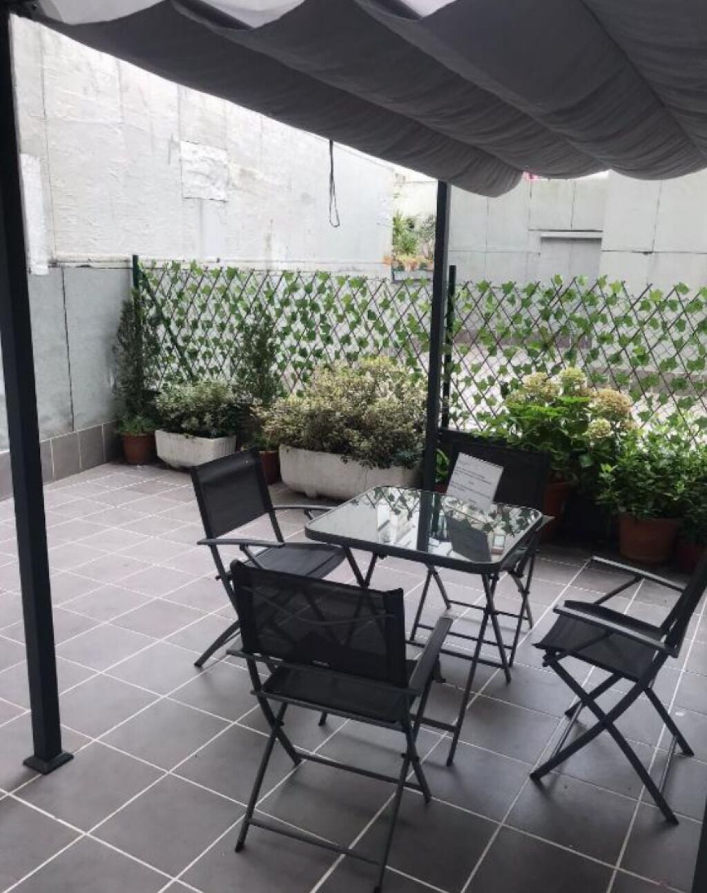 Une terrasse extérieure avec une table et des chaises, entourée de plantes en pot et d’une clôture en treillis.