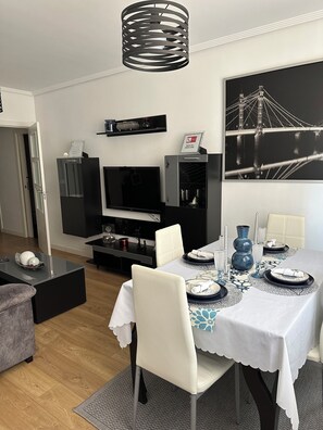 A modern dining area with a table set for four, a black-framed television, and a black and white framed picture on the wall. - Castro Apartment (Castro-Urdiales)