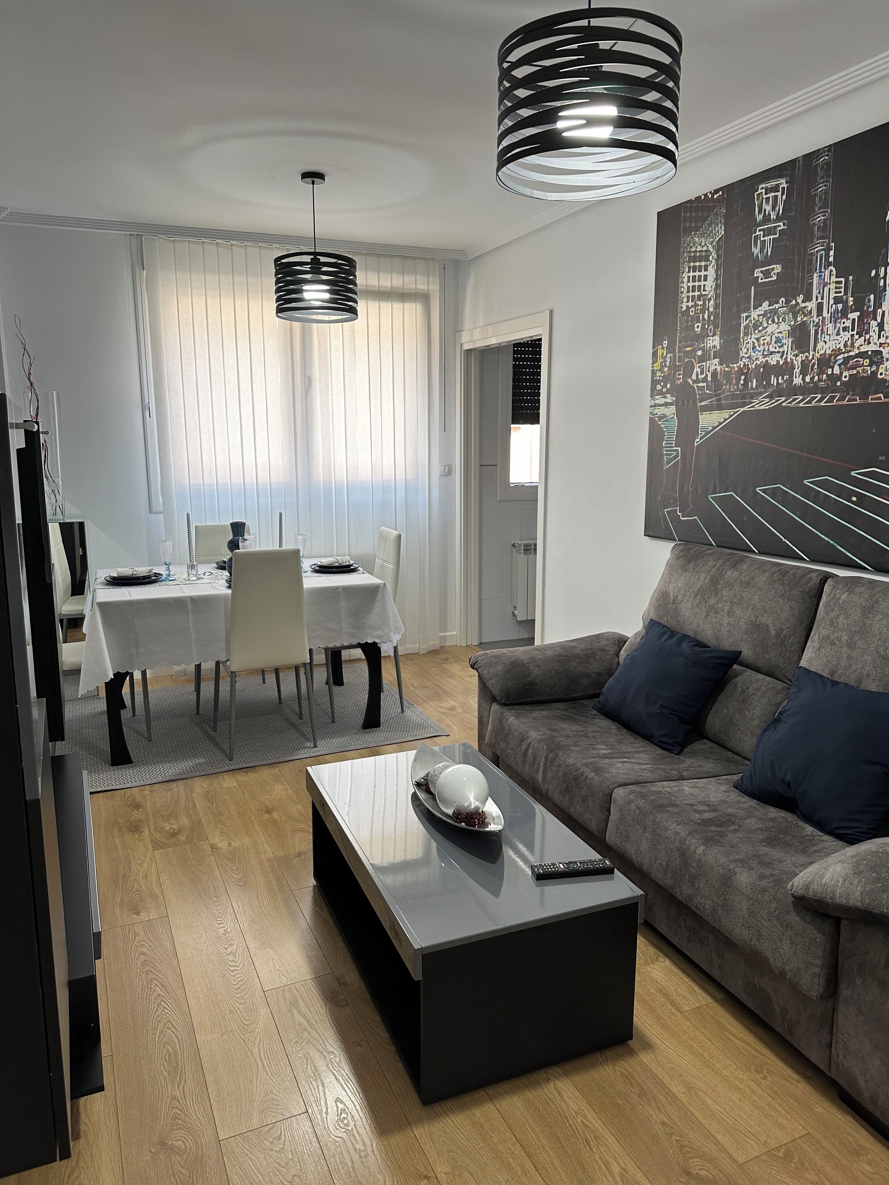 Un salon moderne avec un canapé gris, une table basse et un coin repas comprenant une table et des chaises blanches.